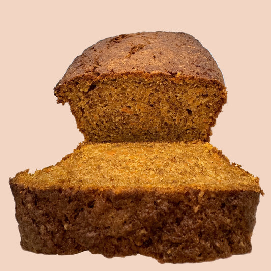 Loaf of carrot cake bread with a slice cut, on a white plate against a light blue background