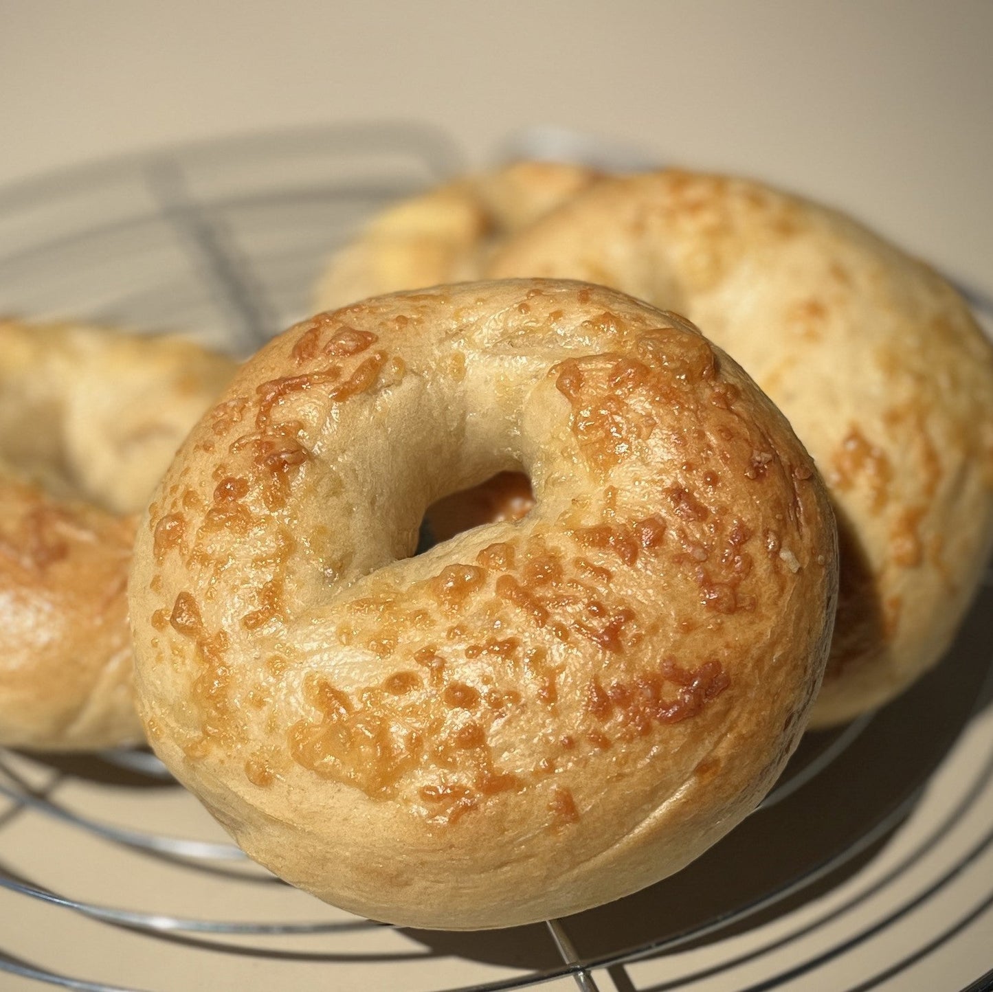Three golden-brown baked Queijo bagels resting on a wire cooling rack at cafeAtaraxia in Parede, Portugal.  The best bagels in Portugal.